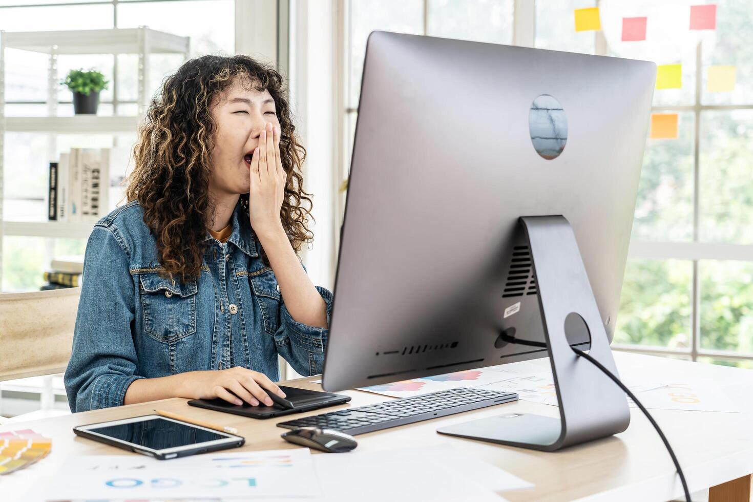 Young asian business woman yawns at office desk in front of laptop. Businesswoman covering mouth out of courtesy chain reaction drowsiness, suffer from lack of sleep photo
