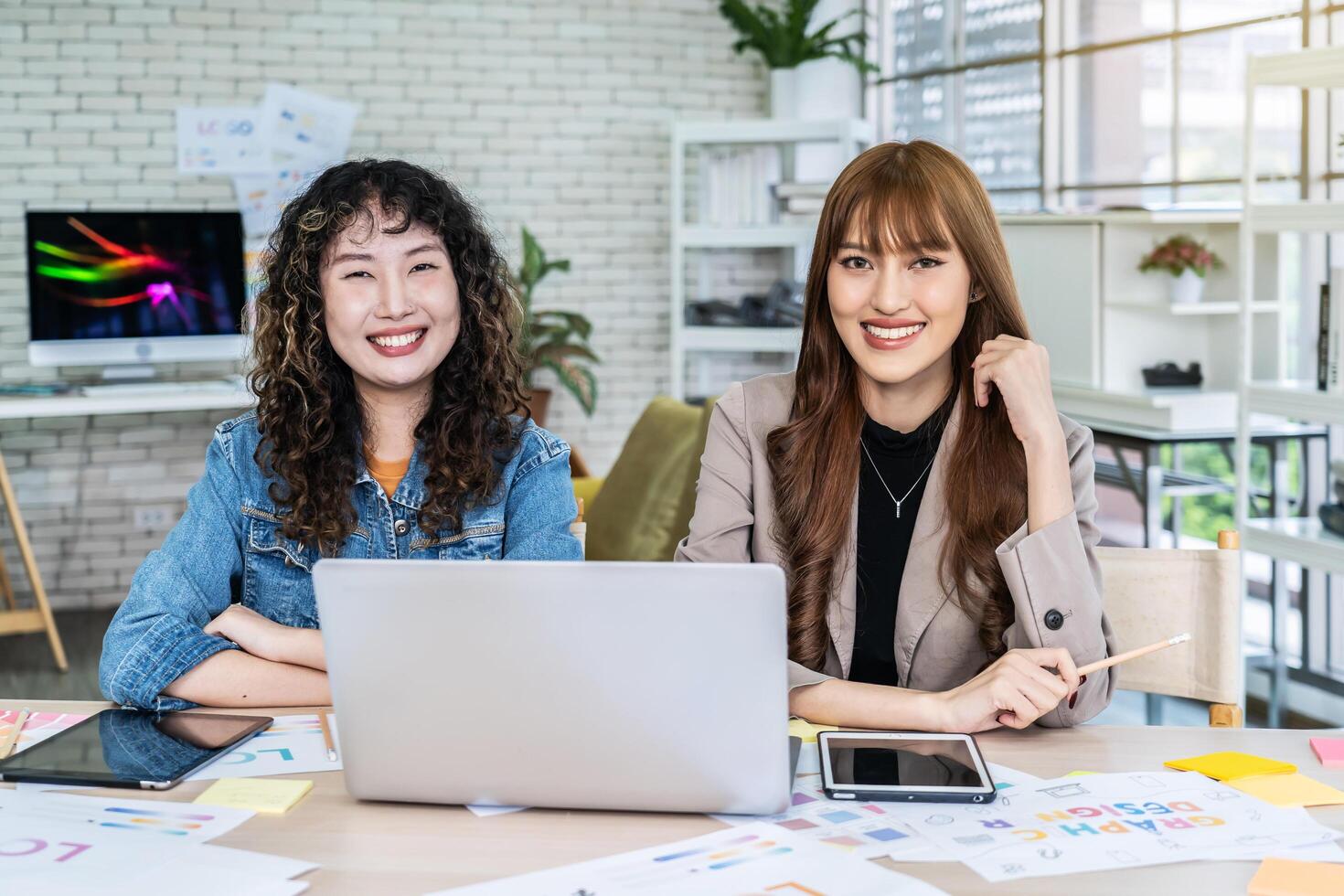Two business young asian woman working in computer laptop together in office with reports, colleagues discuss financial data analyzing documents marketing project result talk business conversation photo