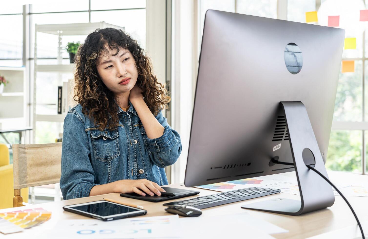Tired fatigued asian girl feel neck discomfort with computer work in office, Young Asia girl development programmer overworked tired painful shoulder neck muscle from office syndrome photo