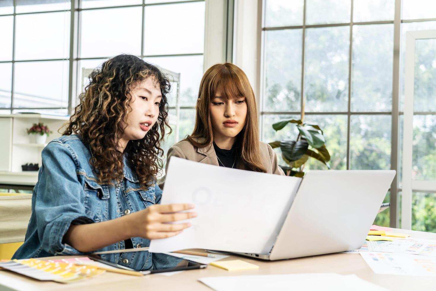 Two business young asian woman working in computer laptop together in office with reports, colleagues discuss financial data analyzing documents marketing project result talk business conversation photo