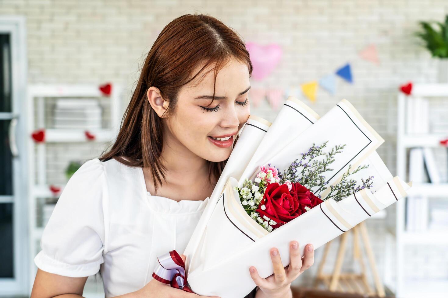 Asian young man surprising his beautiful girlfriend with bouquet of flowers at home, Attractive romantic new marriage couple male and woman spend time to celebrate anniversary and valentine's day photo