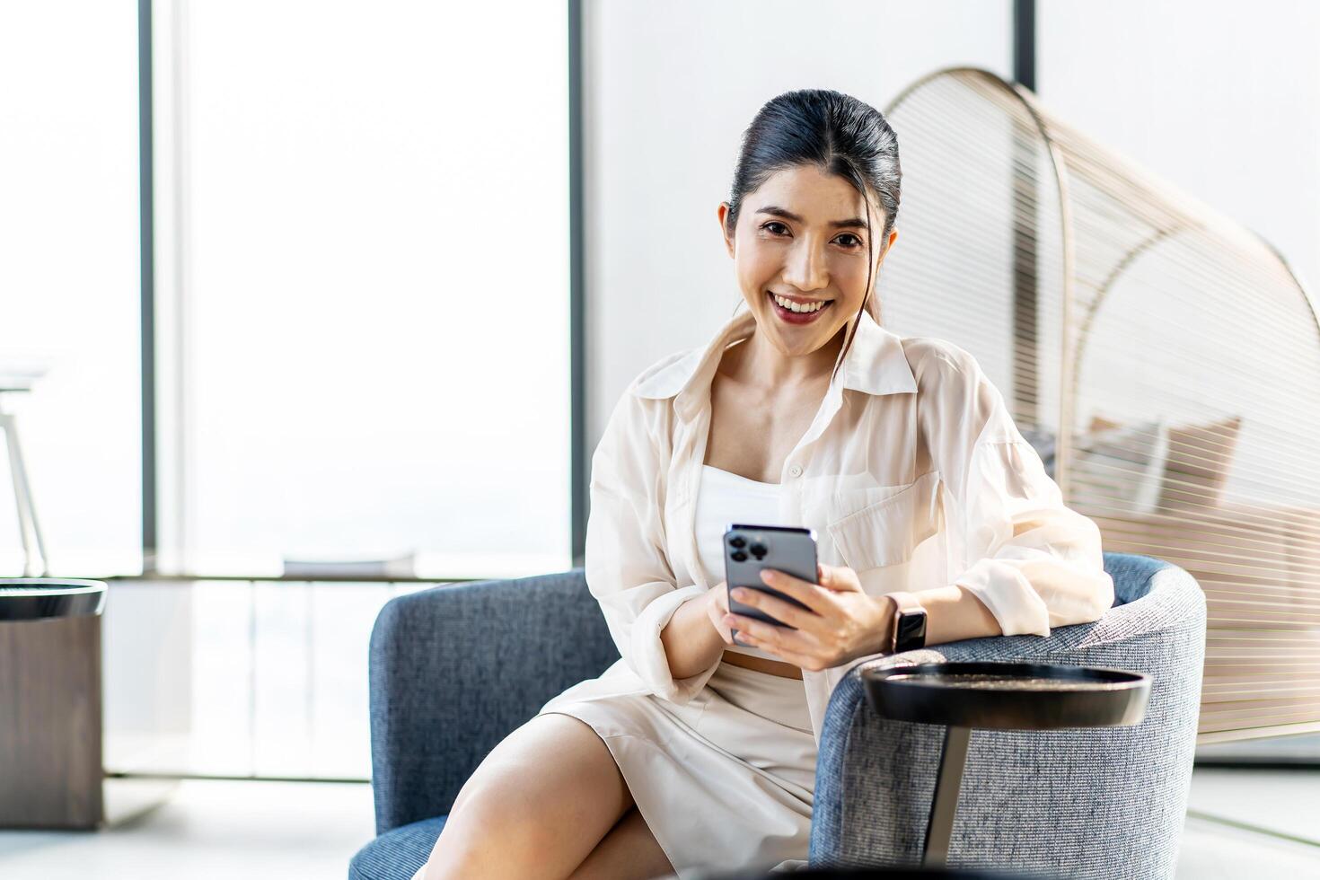 Smiling asian woman hold use smart phone sitting at home. watching social media. Portrait, entertainment, communication, work or study, connection, mobile apps, lifestyle concept. photo