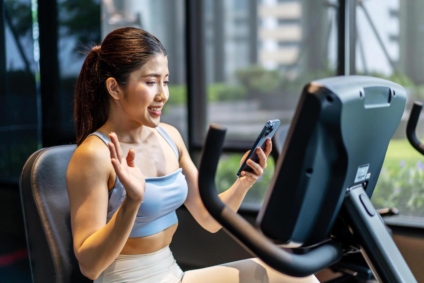 Young asian athletic woman with perfect body wearing sportswear making call with smart phone to friends or family to show her achievements and results while workout in gym, healthy lifestyle photo