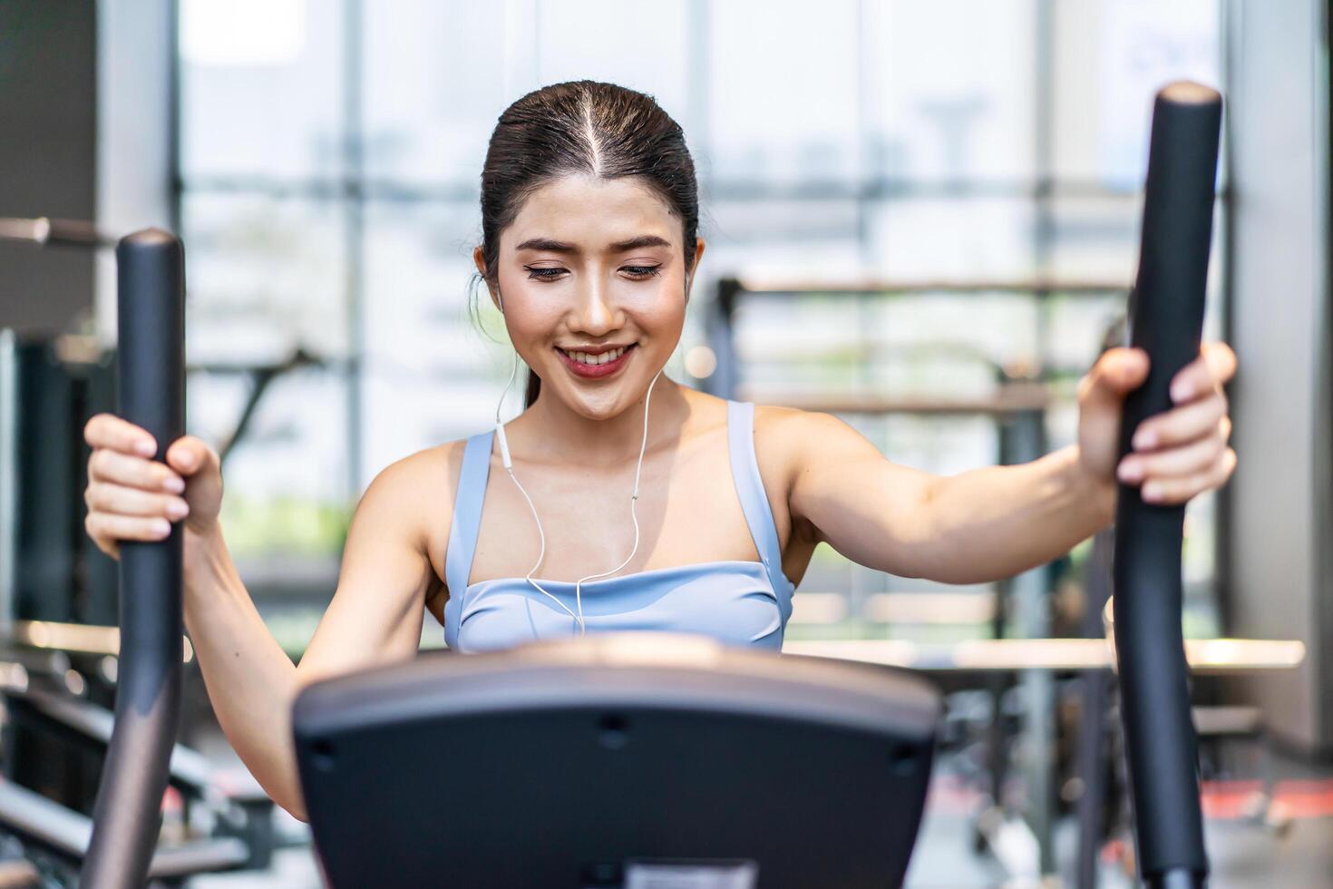 Young asian girl jogging on a treadmill in a gym, Muscular athletes actively training in the gym, Female training at fitness center. Woman exercising cardio workout, exercise lose weight, listen music photo