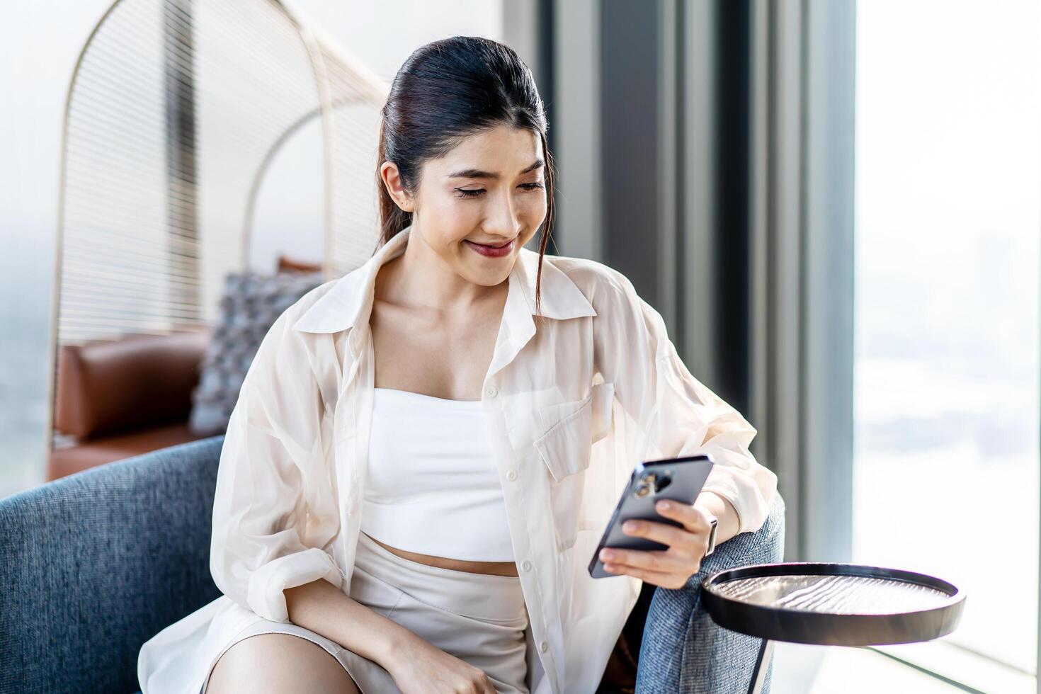 Smiling asian woman hold use smart phone sitting at home. watching social media. Portrait, entertainment, communication, work or study, connection, mobile apps, lifestyle concept. photo