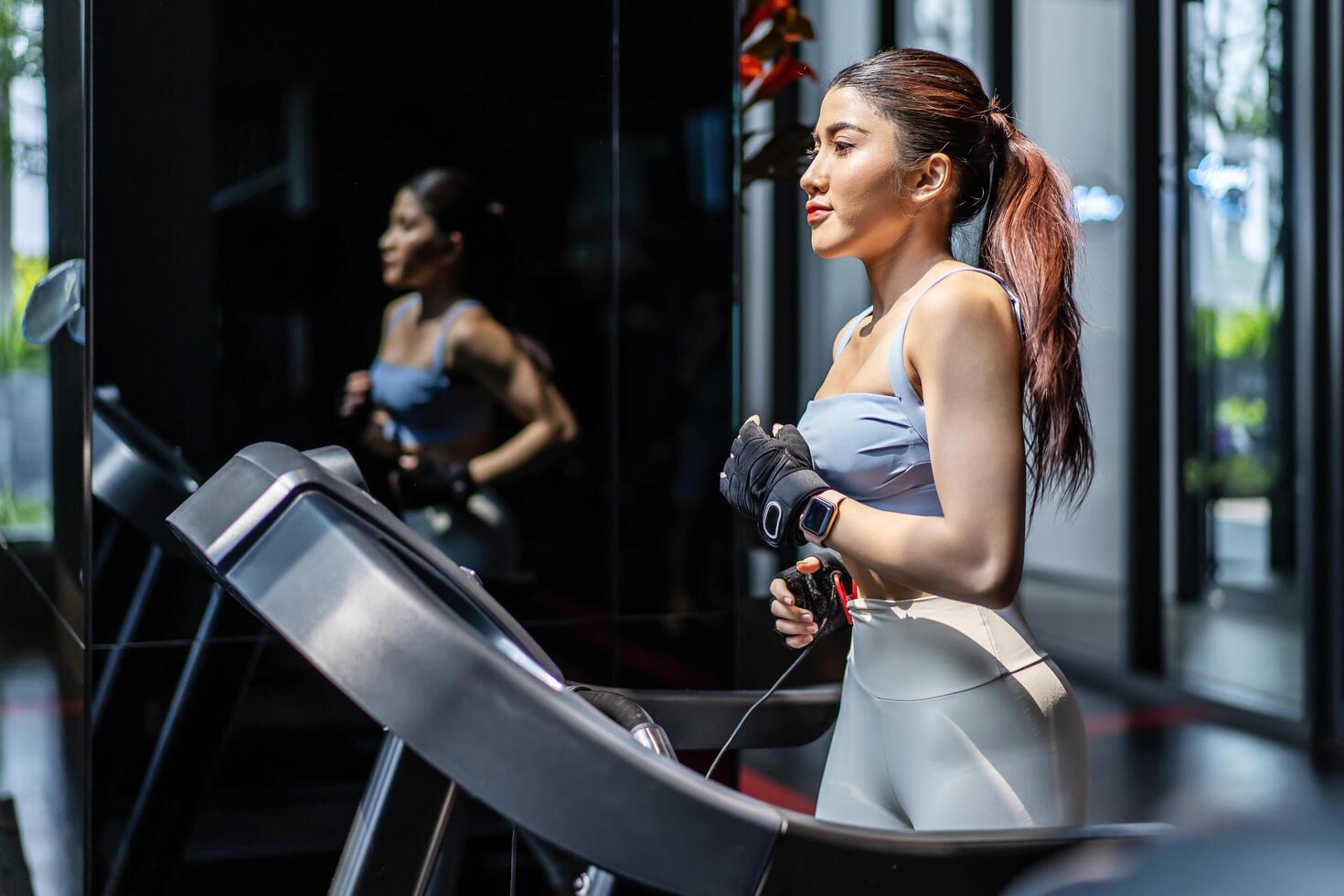 Young asian girl jogging on a treadmill in a gym, close-up, side view, Muscular athletes actively training in the gym, Female training at fitness center. Woman exercising cardio workout photo