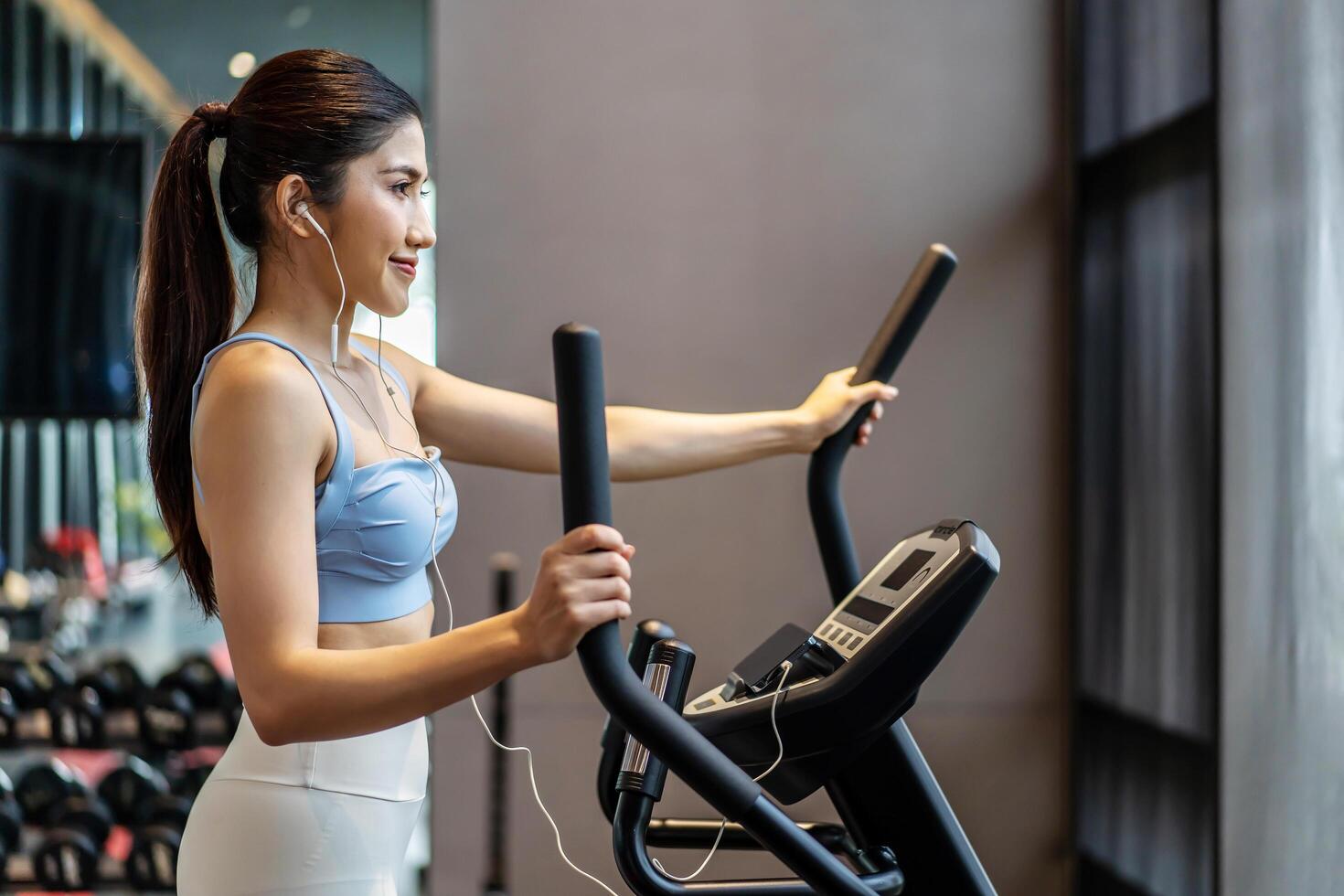 Young asian girl jogging on a treadmill in a gym, Muscular athletes actively training in the gym, Female training at fitness center. Woman exercising cardio workout, exercise lose weight, listen music photo