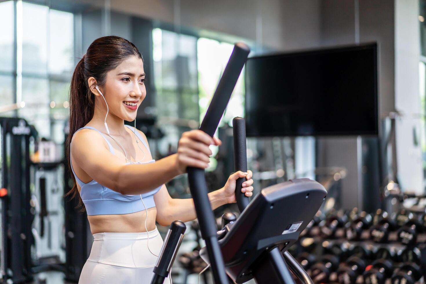 Young asian girl jogging on a treadmill in a gym, Muscular athletes actively training in the gym, Female training at fitness center. Woman exercising cardio workout, exercise lose weight, listen music photo
