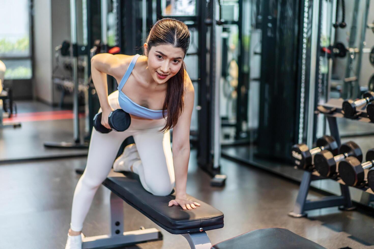 Fitness young asian woman lifting dumbbell in the gym. Morning exercise, Slim young beautiful girl warming up with weights in health club. photo