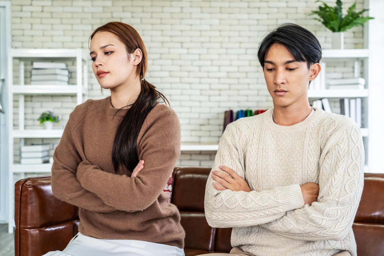 Photo of resentful asian guy and girl acting like arguing couple and not speaking to each other, while sitting together on couch at home