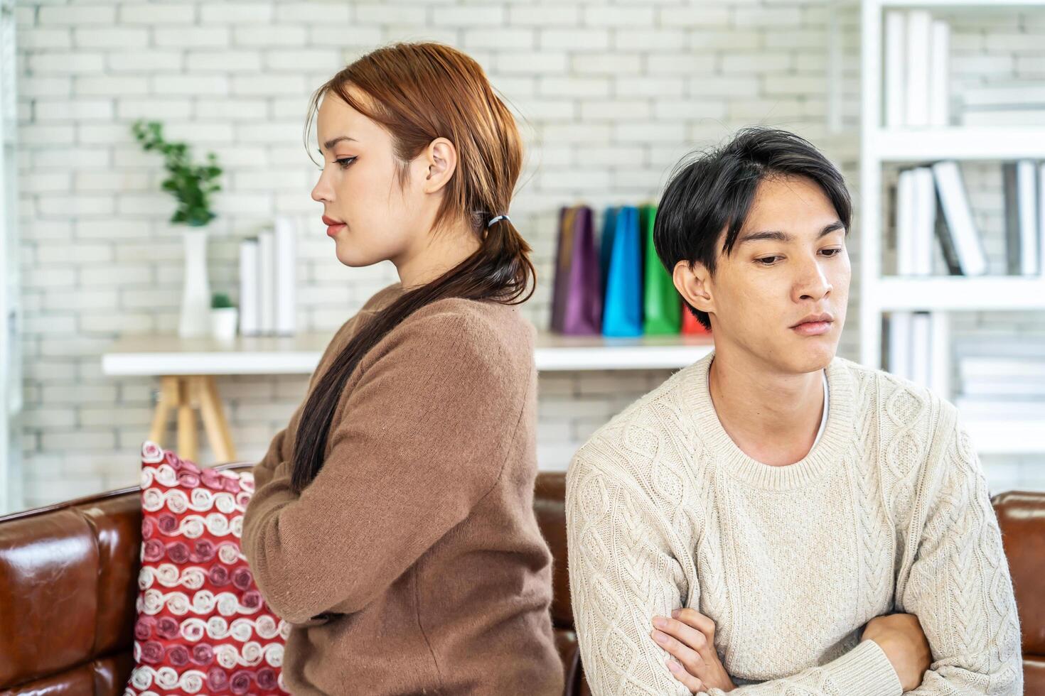 Photo of resentful asian guy and girl acting like arguing couple and not speaking to each other, while sitting together on couch at home