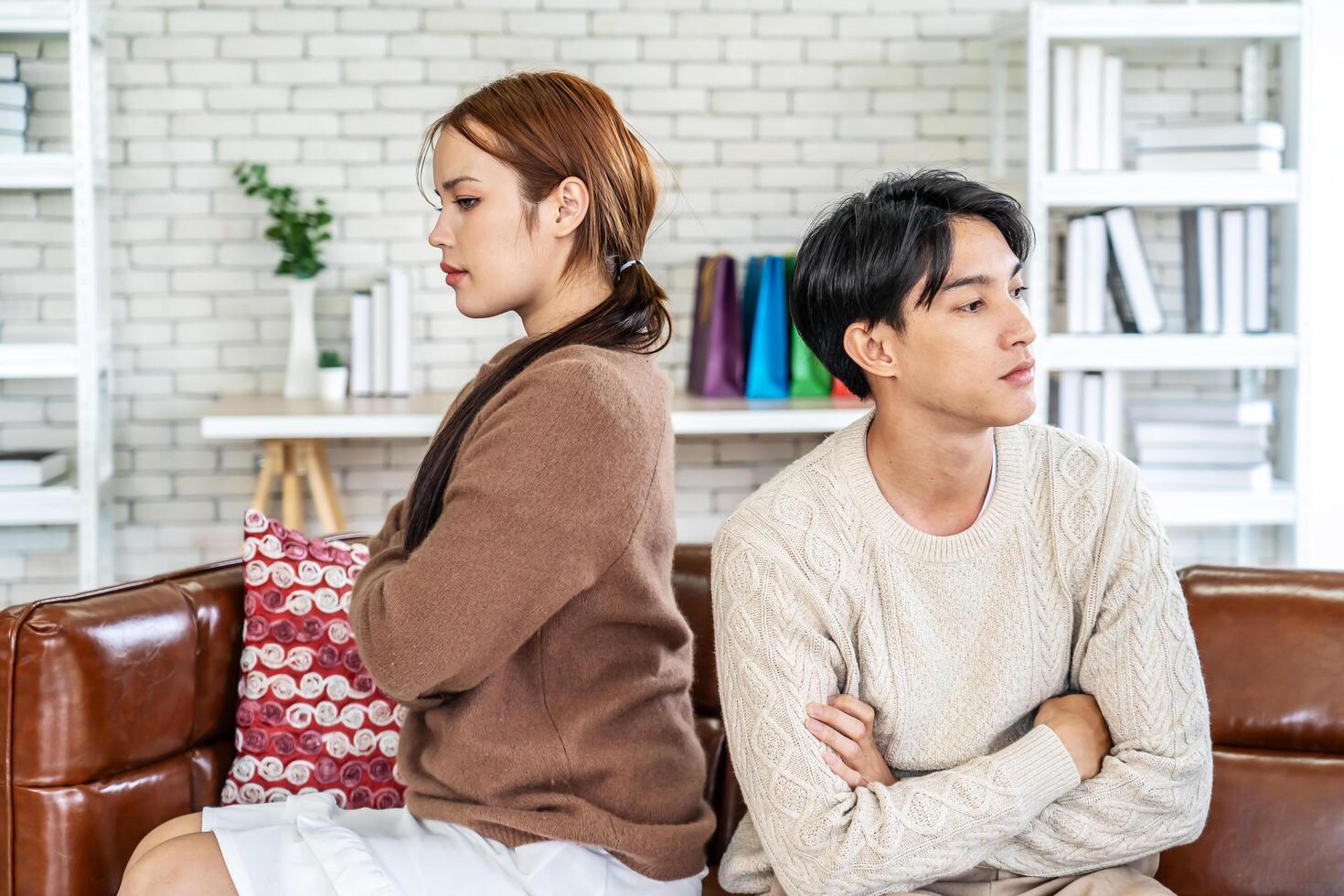 Photo of resentful asian guy and girl acting like arguing couple and not speaking to each other, while sitting together on couch at home