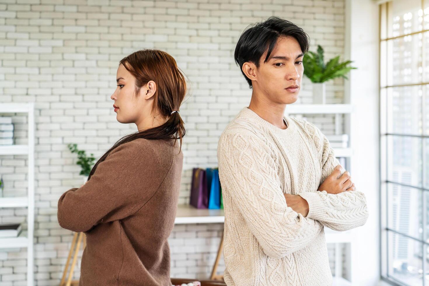 Photo of resentful asian guy and girl acting like arguing couple and not speaking to each other, while standing together in living room at home