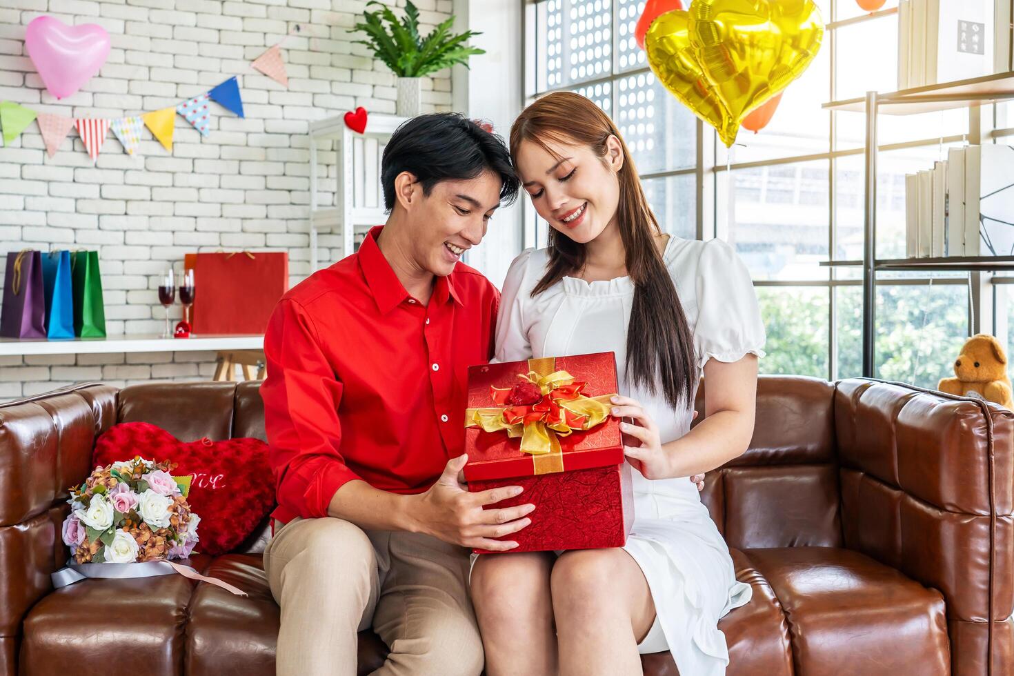 Excited young asian woman opening gift box receiving good unexpected present from husband at home, loving generous boyfriend making romantic surprise to attractive girlfriend on Valentines day photo