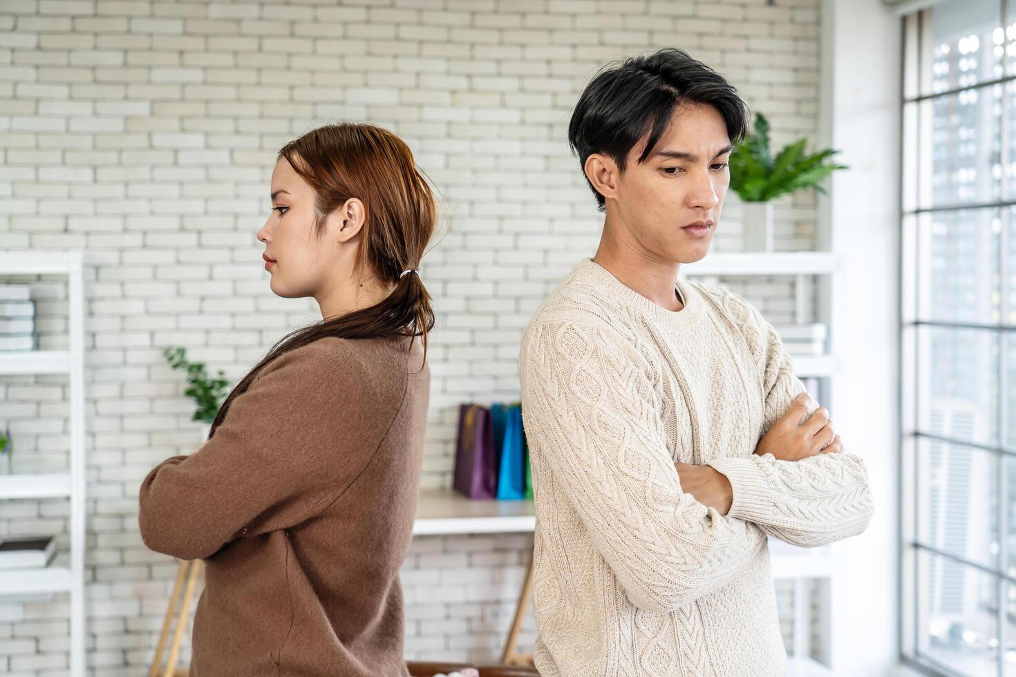 Photo of resentful asian guy and girl acting like arguing couple and not speaking to each other, while standing together in living room at home