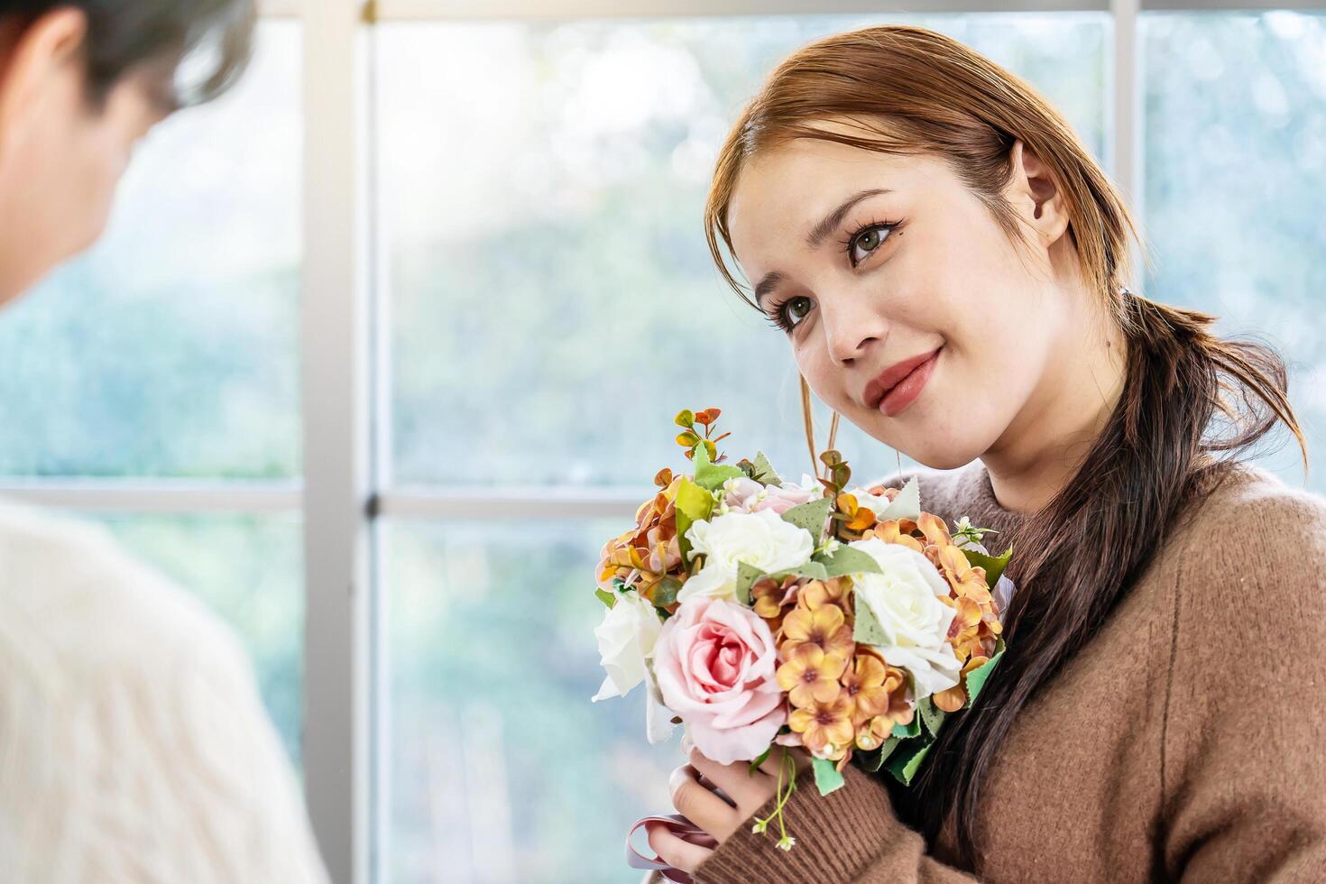 Asian young man surprising his beautiful girlfriend with bouquet of flowers at home, Attractive romantic new marriage couple male and woman spend time to celebrate anniversary and valentine's day photo