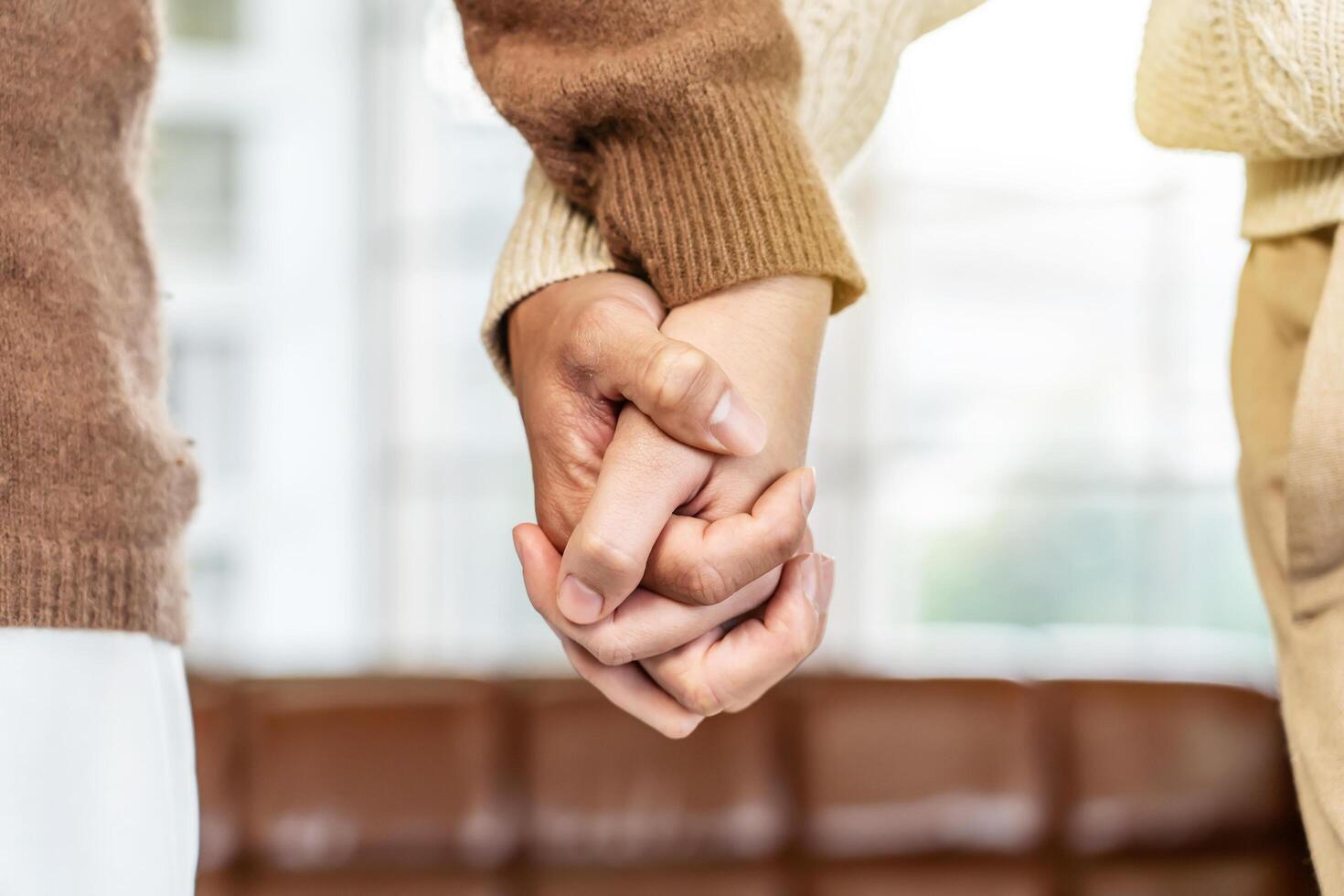 Close up of hand young happy loving couple guy and girl standing in front of big window, back to camera front view of an affectionate couple looking out of window while holding hand photo