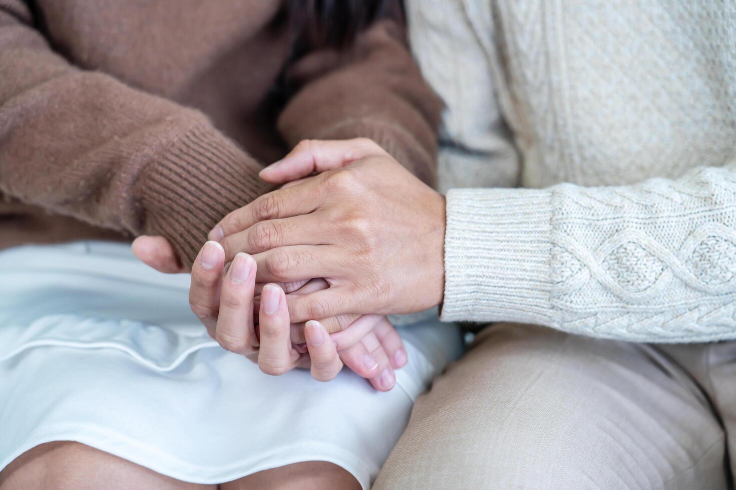 Closeup, couple and holding hands while resting on couch at home, to forgive, love and care with empathy at home. Life partner, helping hand and support of man, woman and hope for kindness photo