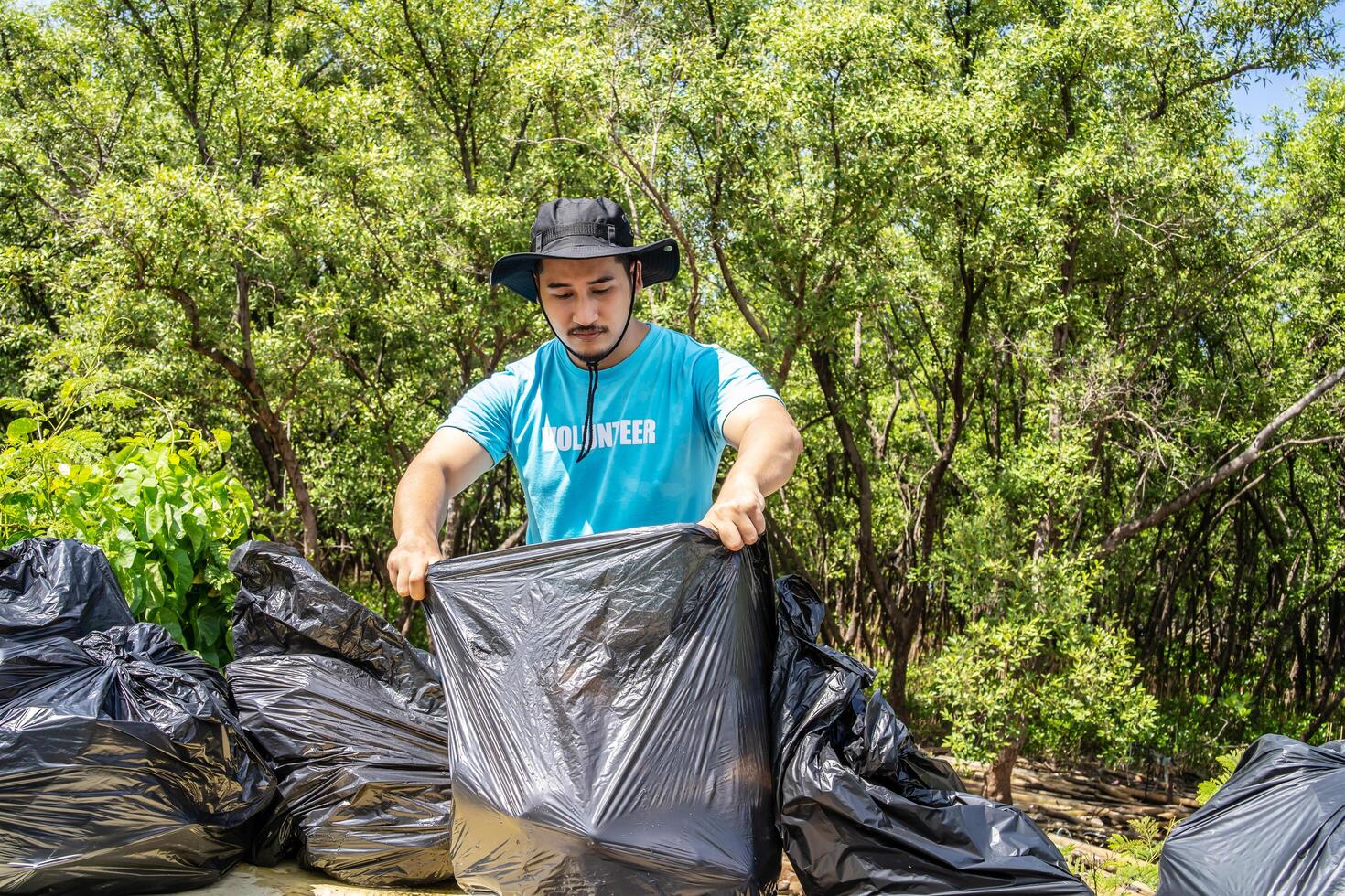 One volunteers in work overalls collect garbage in forest in plastic bag. Close-up during action. Cleaning of nature from waste. Environmental assistance. Garbage collection in forest photo