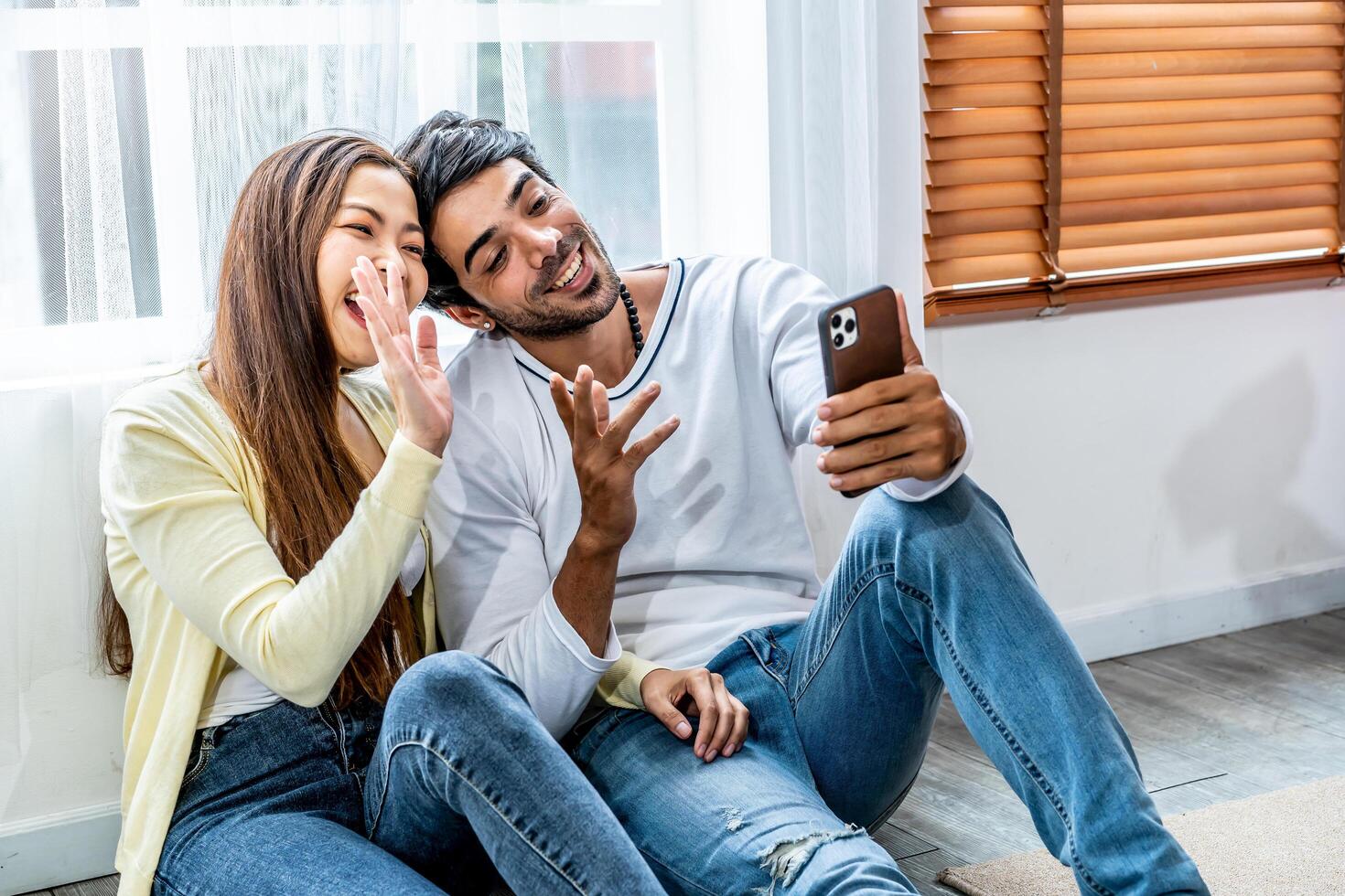 Relaxed young interracial couple or friends say hi and talking in conference by mobile phone together in living room at home, Happy young man and woman with smartphone photo