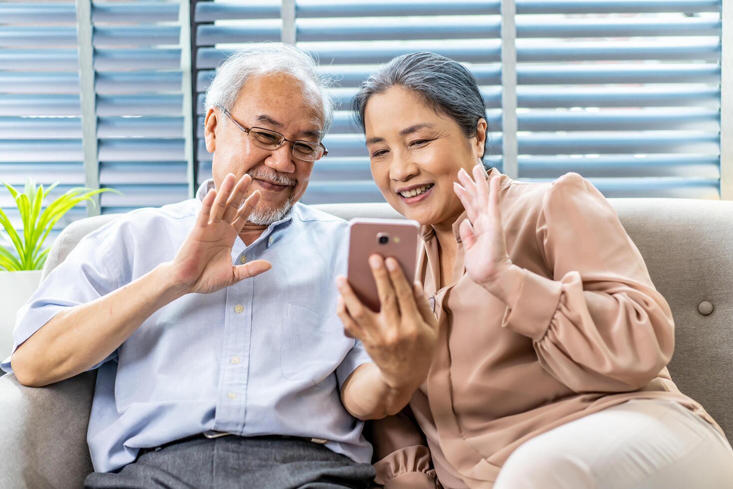 Happy elderly retired couple making call with mobile phone, gesturing hi, having pleasant conversation,chatting with grown up children grandchildren using wireless internet connection at home photo