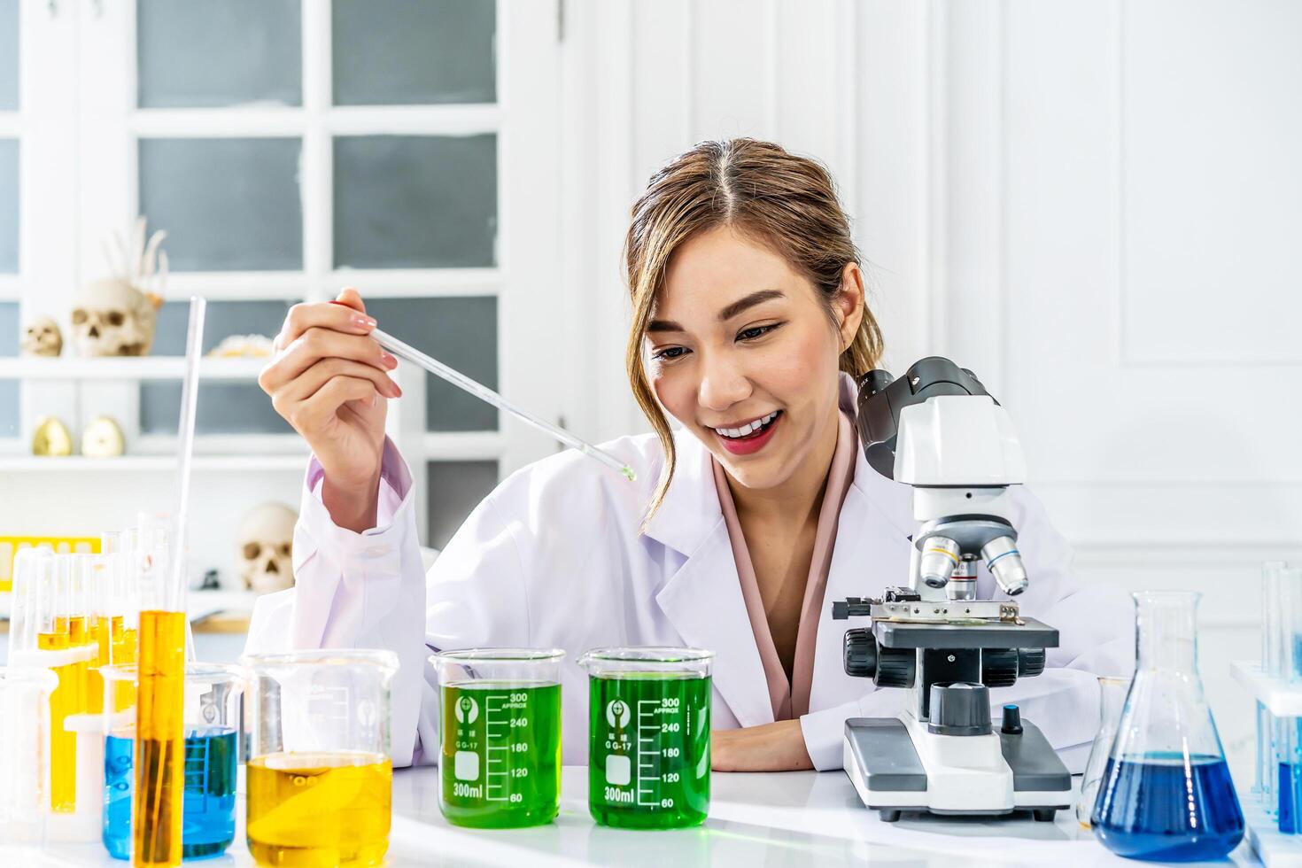 Smiling young asian woman wearing scientist uniform working at scientist laboratory with measuring liquid at laboratory photo