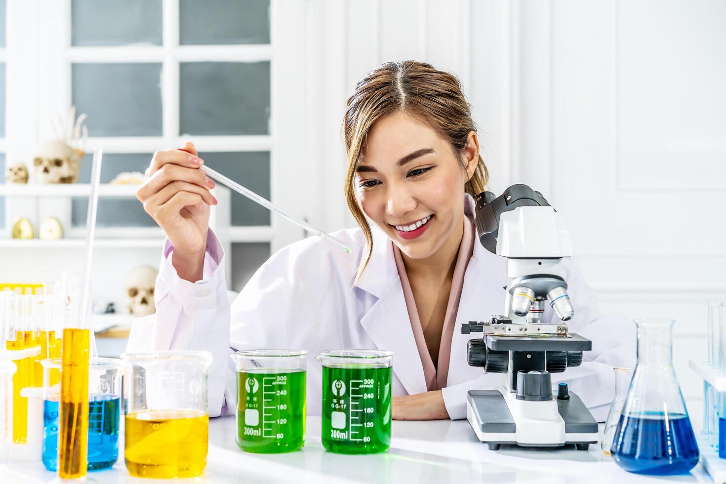 Smiling young asian woman wearing scientist uniform working at scientist laboratory with measuring liquid at laboratory photo