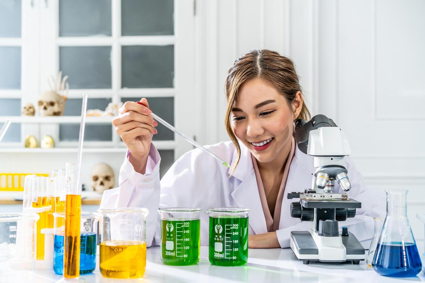 Smiling young asian woman wearing scientist uniform working at scientist laboratory with measuring liquid at laboratory photo