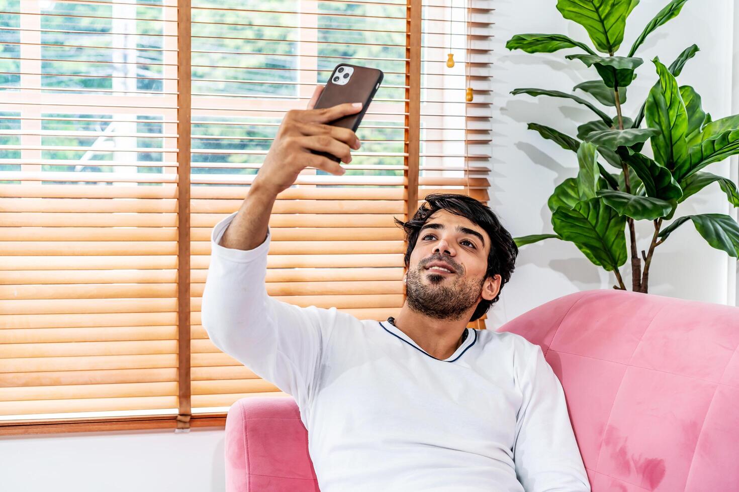 Cool gadget and app. Young smiling guy holding mobile phone, typing sms message, resting on sofa in living room, Texting And Browsing Internet, surfing web, using app, Networking In Social Media photo
