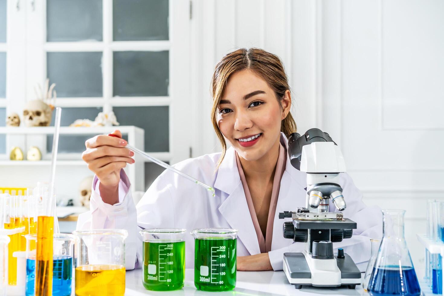 Young asian woman wearing scientist uniform working at scientist laboratory looking at the camera smiling with measuring liquid at laboratory photo
