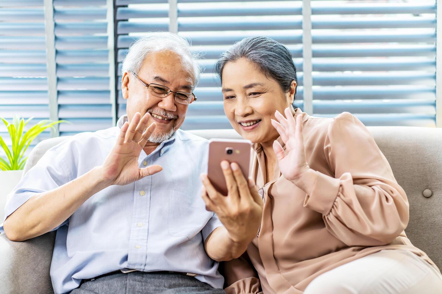 Happy elderly retired couple making call with mobile phone, gesturing hi, having pleasant conversation, chatting with grown up children grandchildren using wireless internet connection at home photo