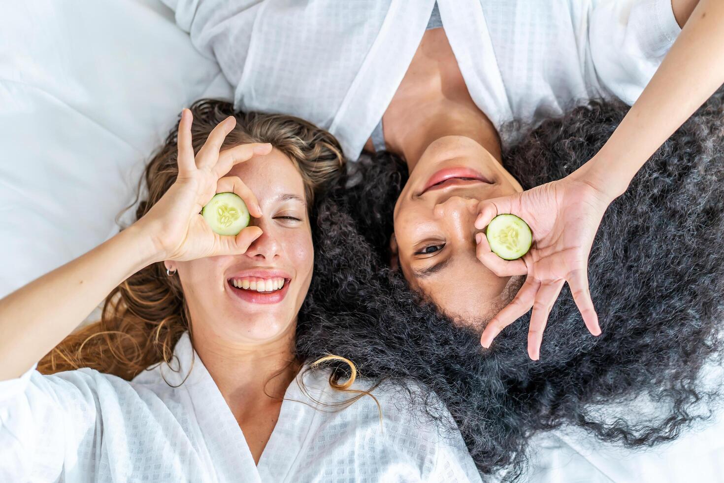 Young smiling woman wear white shirt pajama she lying sit in bed with cucumber slices rest relax spend time in bedroom, Skin care wellbeing photo