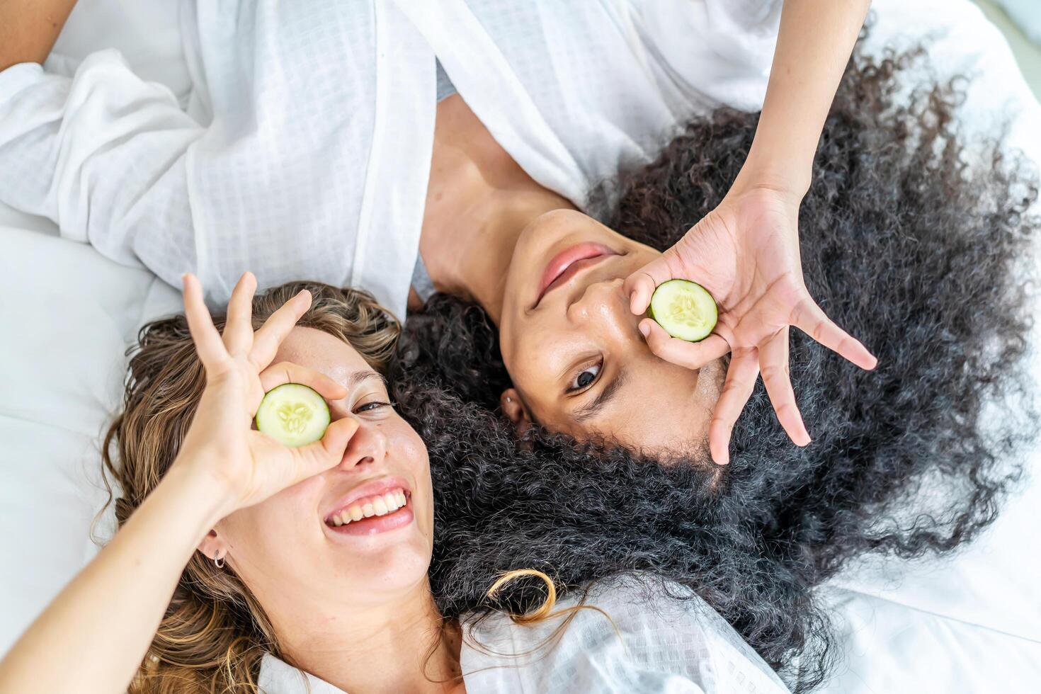Young smiling woman wear white shirt pajama she lying sit in bed with cucumber slices rest relax spend time in bedroom, Skin care wellbeing photo