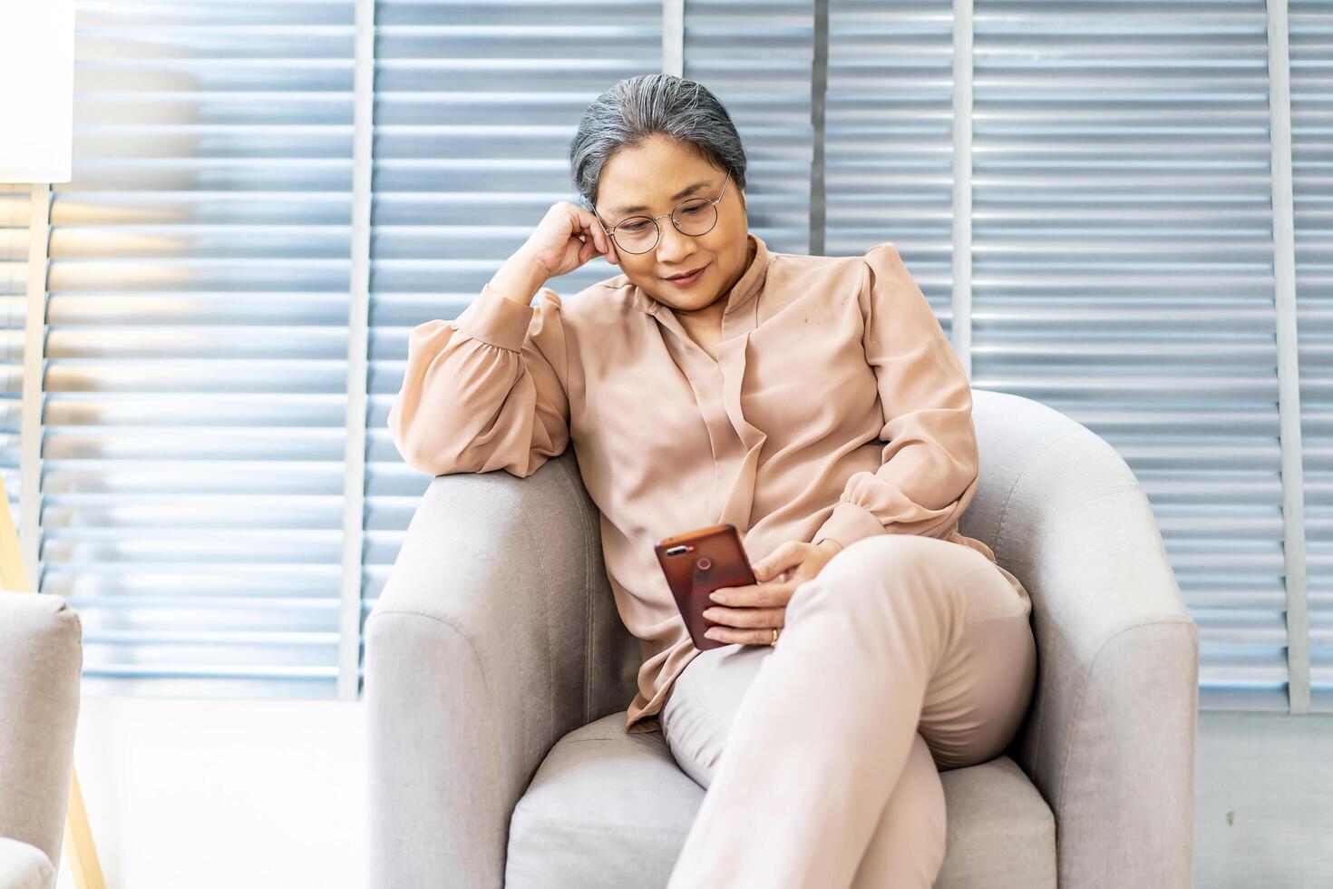 Pleasant senior older lady resting on couch at home, older middle aged female customer holding smartphone using mobile app, texting message, search ecommerce offers on cell phone technology device photo
