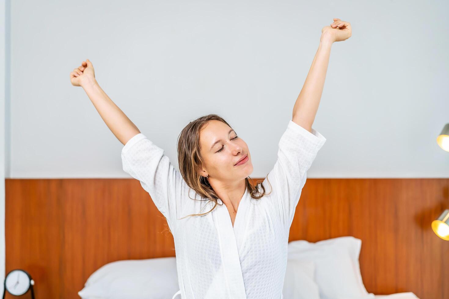 Caucasian beautiful girl in pajamas wake up in the morning with happiness. Attractive young woman smiling, feel happy and relax then stretching body after getting up from sleep on bed in bedroom photo