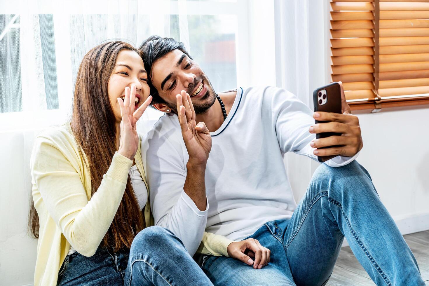 Relaxed young interracial couple or friends say hi and talking in conference by mobile phone together in living room at home, Happy young man and woman with smartphone photo
