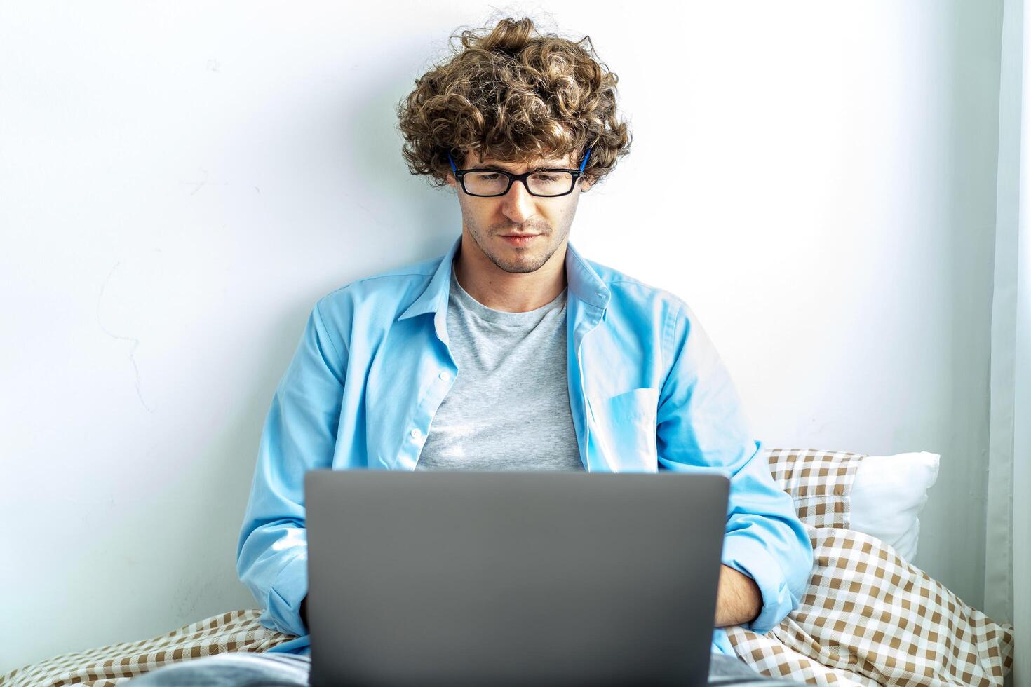 work from home. young caucasian man working on computer laptop. study online listening learning education course conference calling sit laying down on bed elearning concept, freelancer at home photo