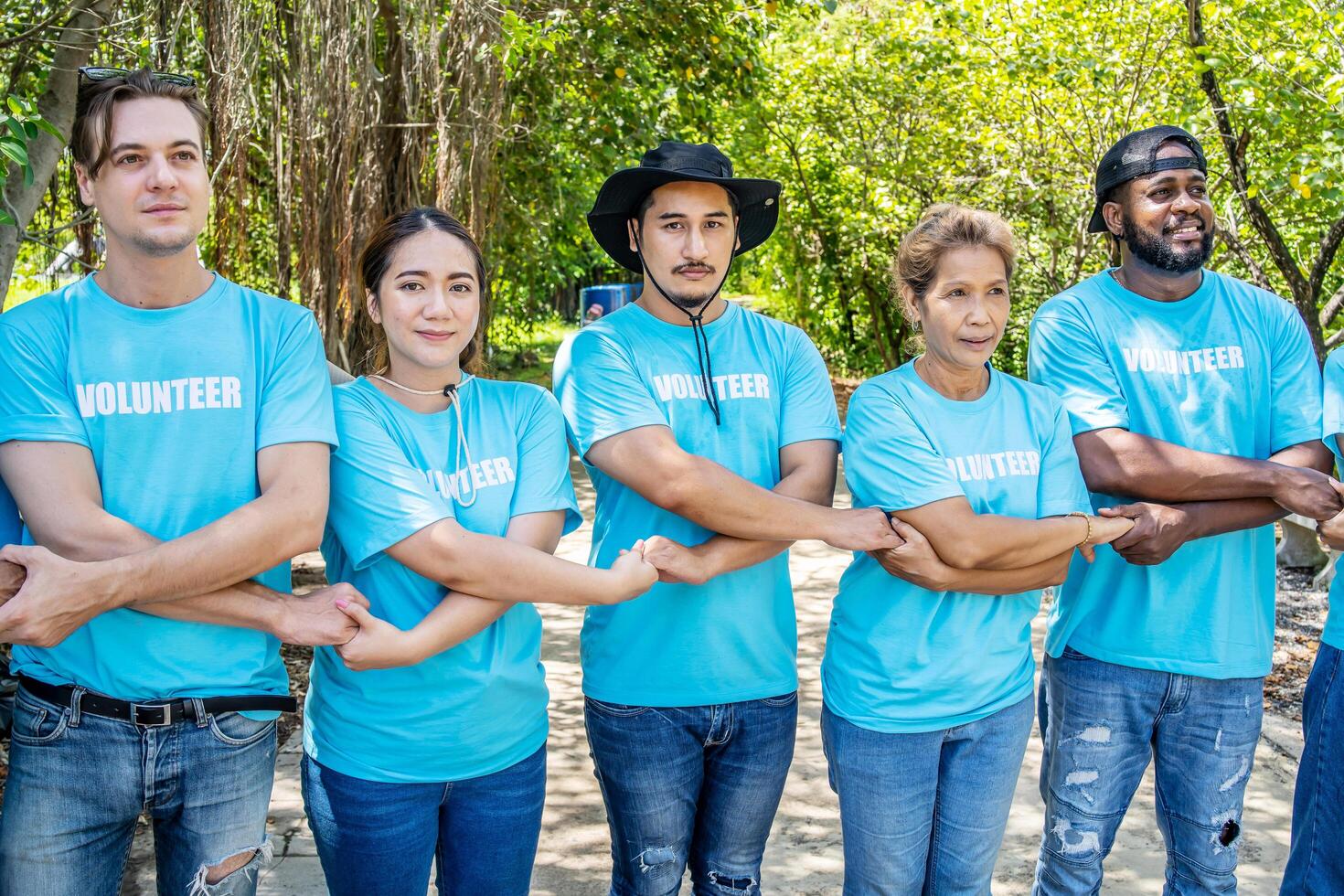 Portrait of smiling male and female volunteers standing with arms around. Multiracial group of confident activists are in park. They are volunteering for environmental cleanup. photo