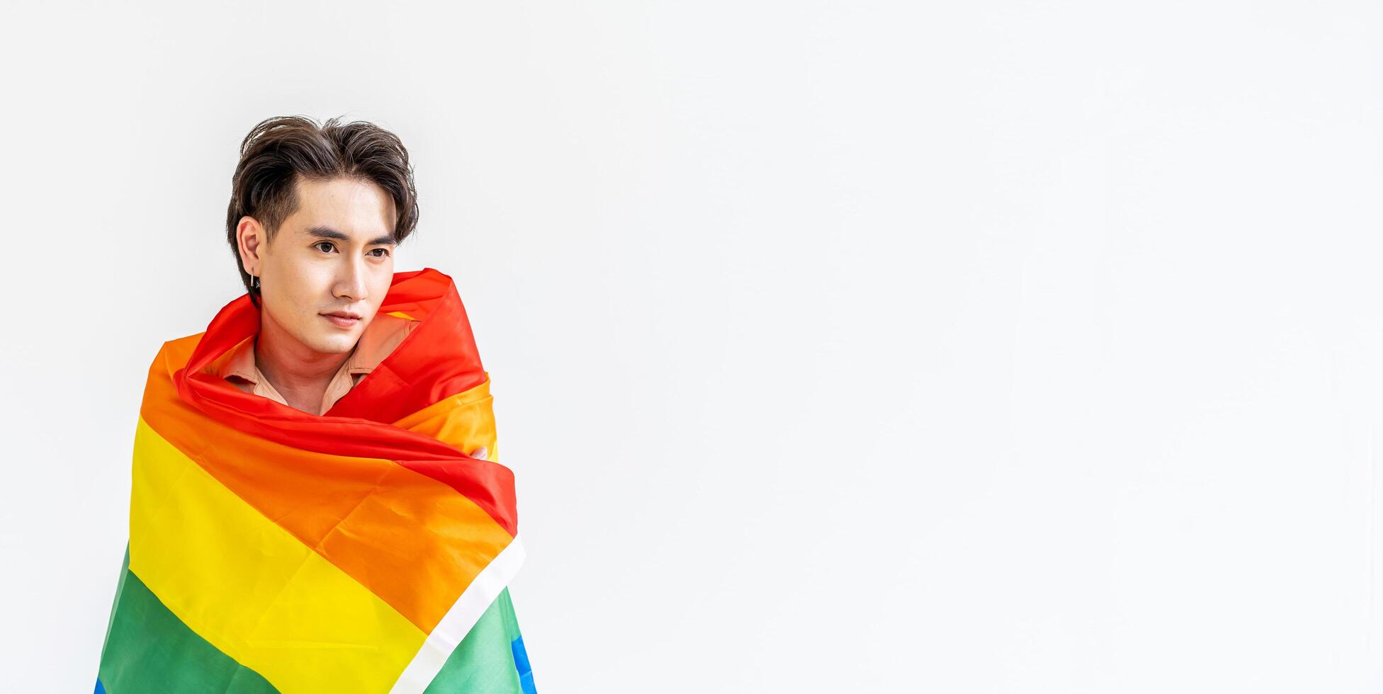 Portrait of transgender or gay man smiling in front of camera taking cover with lgbt flag on white background with copy space. People lifestyle fashion lgbtq concept photo