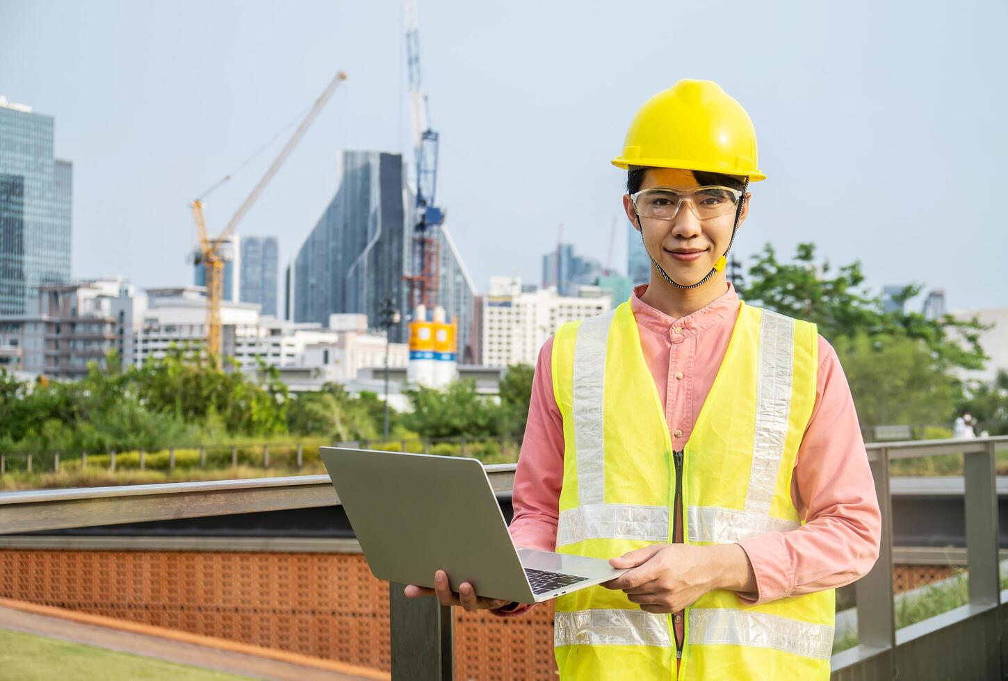 Engineer or construction worker Asian man is holding the laptop and working concentrated at building plan, Hard hat help protect with operation photo