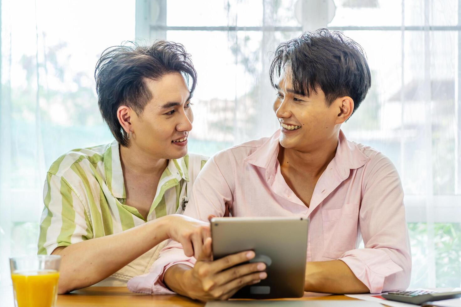 Attractive male lgbtq collegues working together with using digital tablet and paper showing graphic chart in living room, Lgbt love concept photo