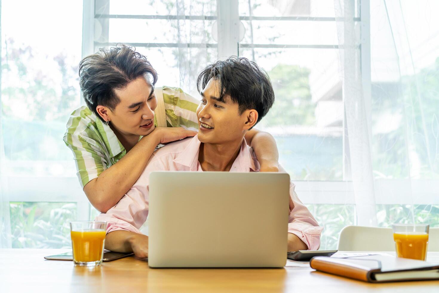 Young asian gay hugging and takes care of his boyfriend while working on his laptop at home, lgbt couple photo