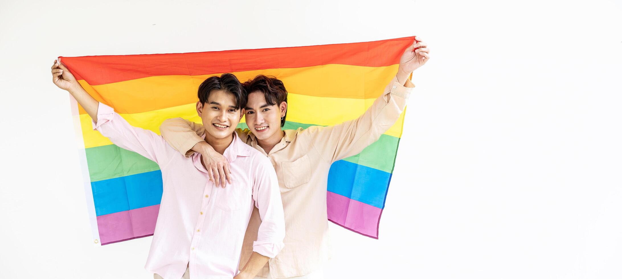 Portrait of Happy gay couple showing their love with rainbow flag. holding each other and holding up an LGBTQ flag, They are laughing, LGBT and love concept. photo