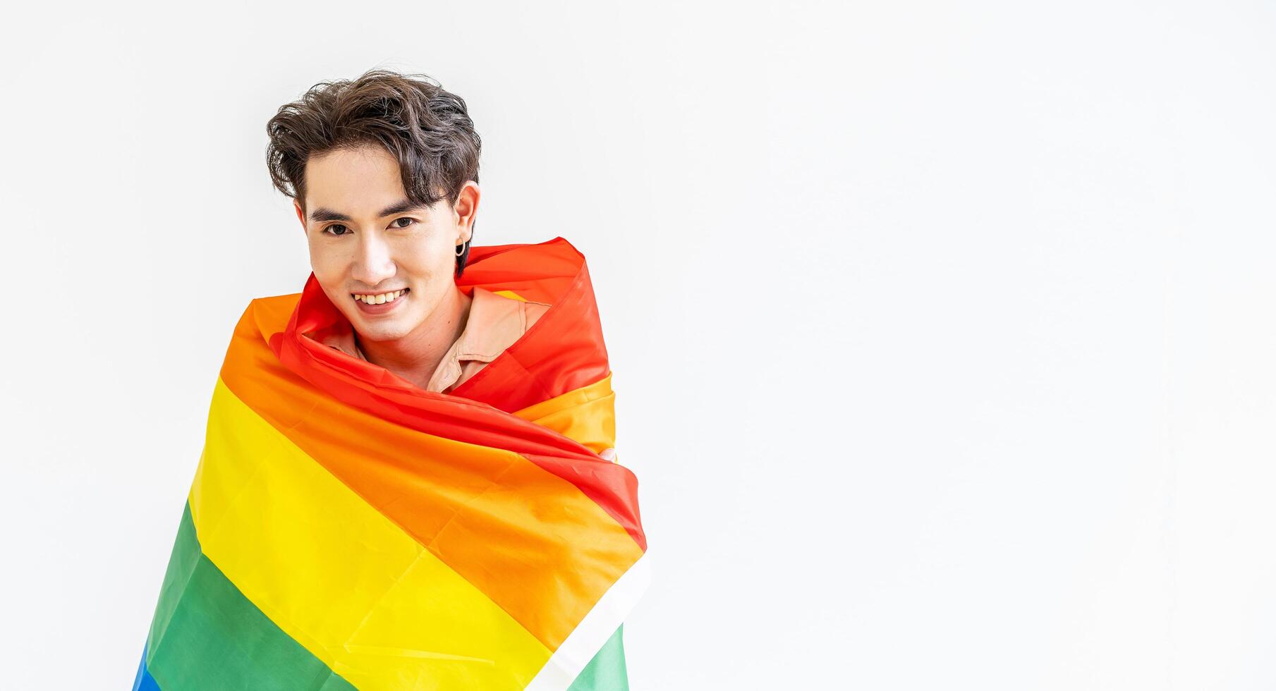Portrait of transgender or gay man smiling in front of camera taking cover with lgbt flag on white background with copy space. People lifestyle fashion lgbtq concept photo