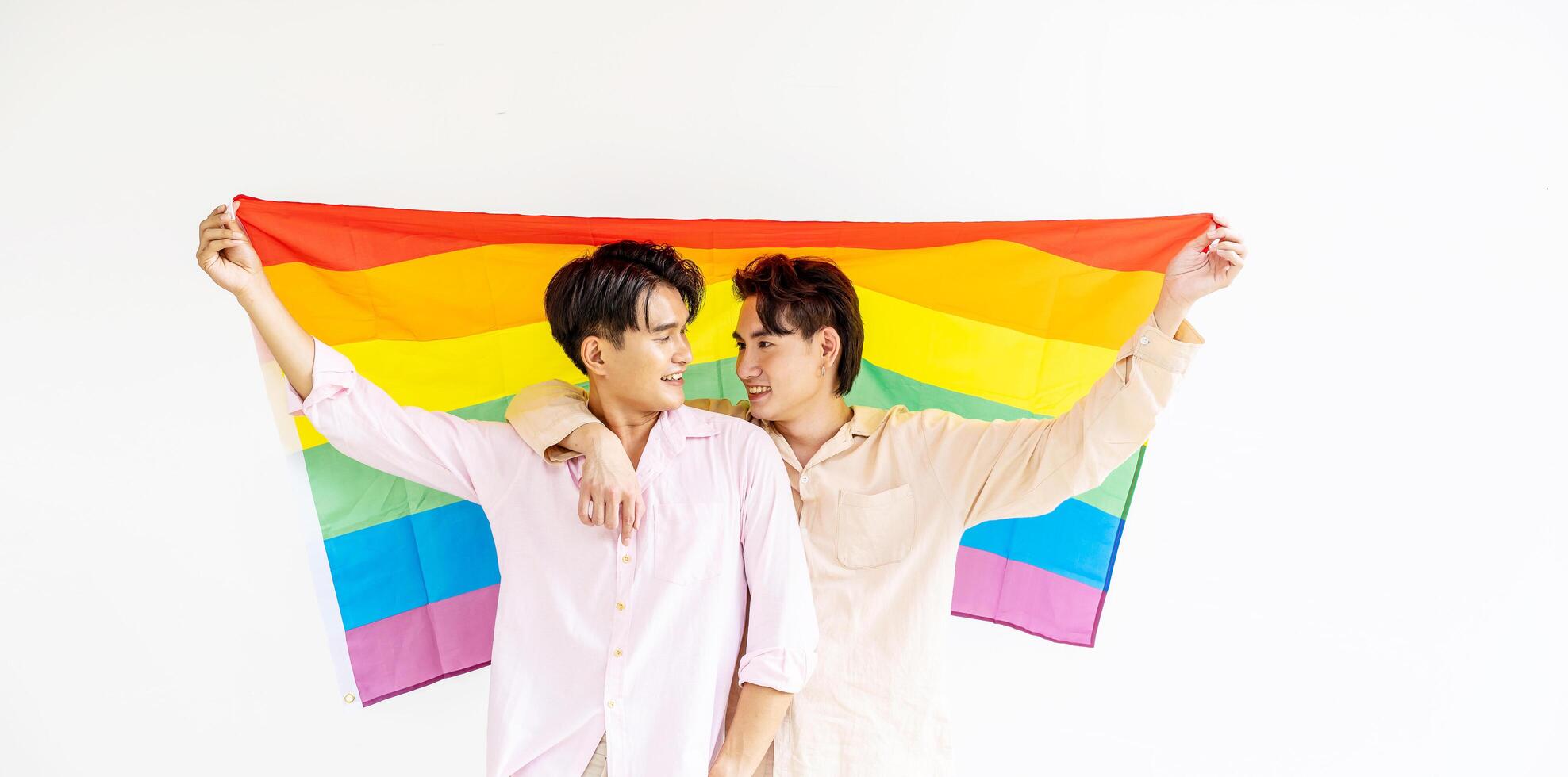 Portrait of Happy gay couple showing their love with rainbow flag. holding each other and holding up an LGBTQ flag, They are laughing, LGBT and love concept. photo