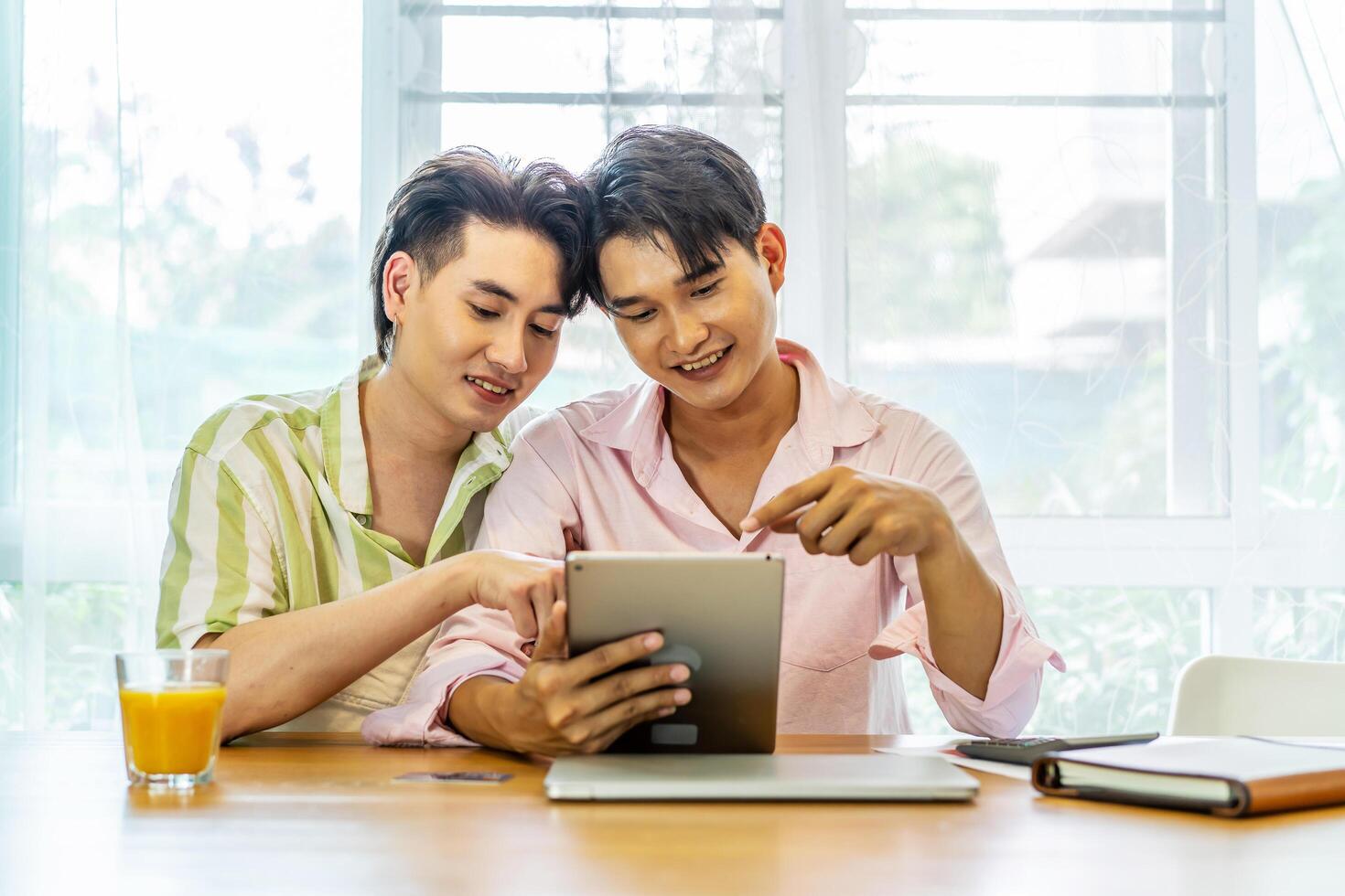 Attractive male lgbtq collegues working together with using digital tablet and paper showing graphic chart in living room, Lgbt love concept photo