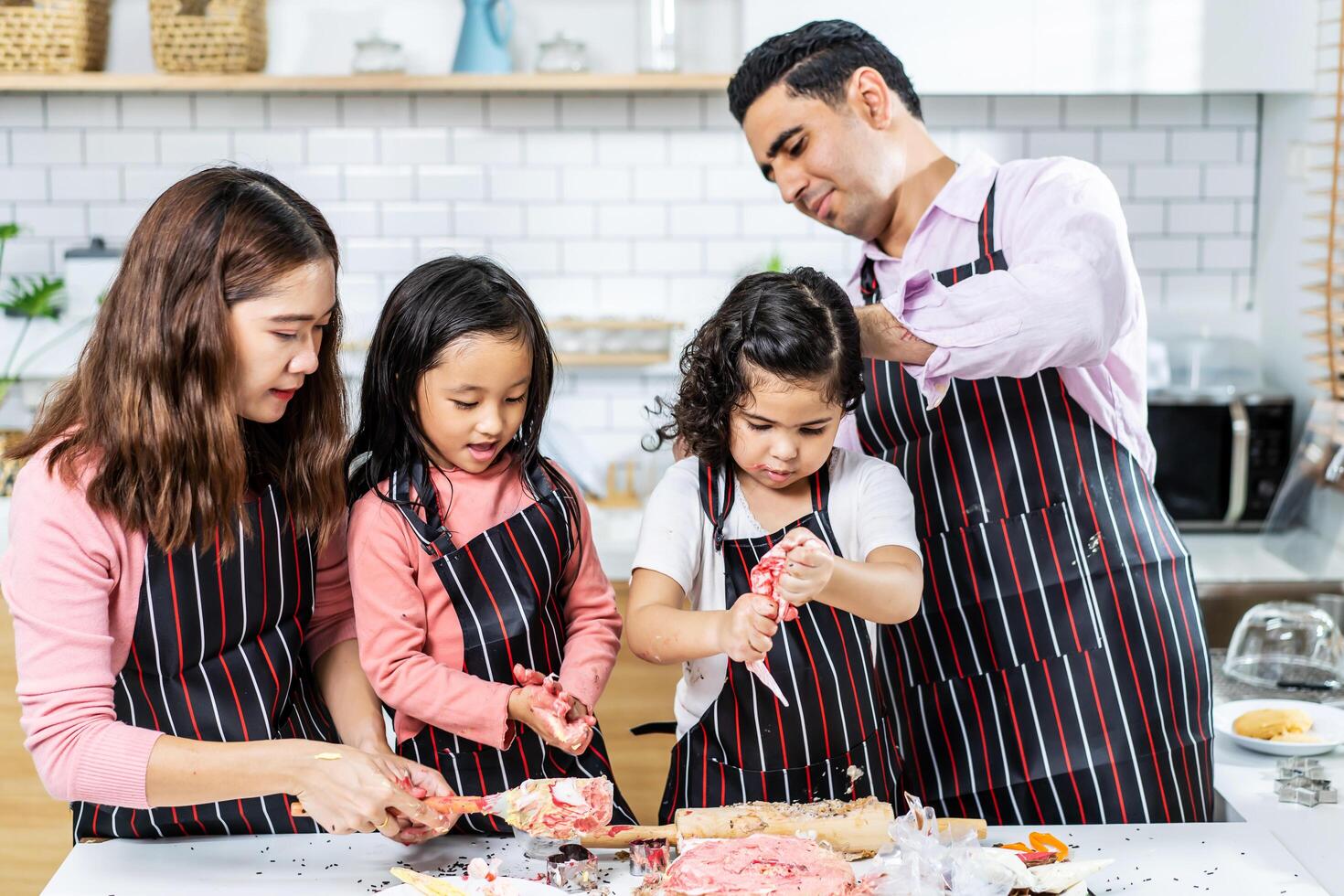 grupo de cuatro diverso familia, asiático y árabe preescolar niño persona hacer pastel Cocinando en cocina, padre madre enseñando pequeño linda hija preparar decoración bonito con divertido, crema lío terminado cara foto