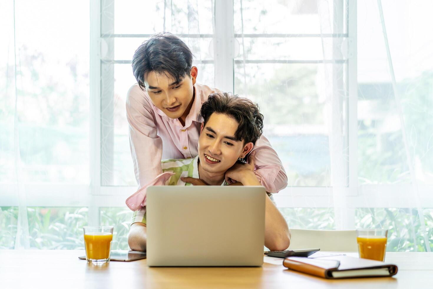 Young asian gay hugging and takes care of his boyfriend while working on his laptop at home, lgbt couple photo