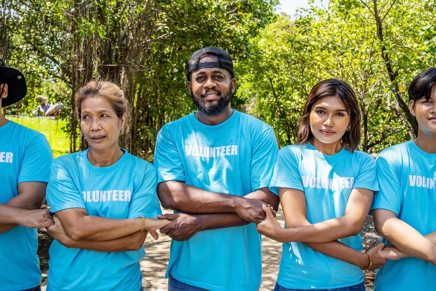 Portrait of smiling male and female volunteers standing with arms around. Multiracial group of confident activists are in park. They are volunteering for environmental cleanup. photo