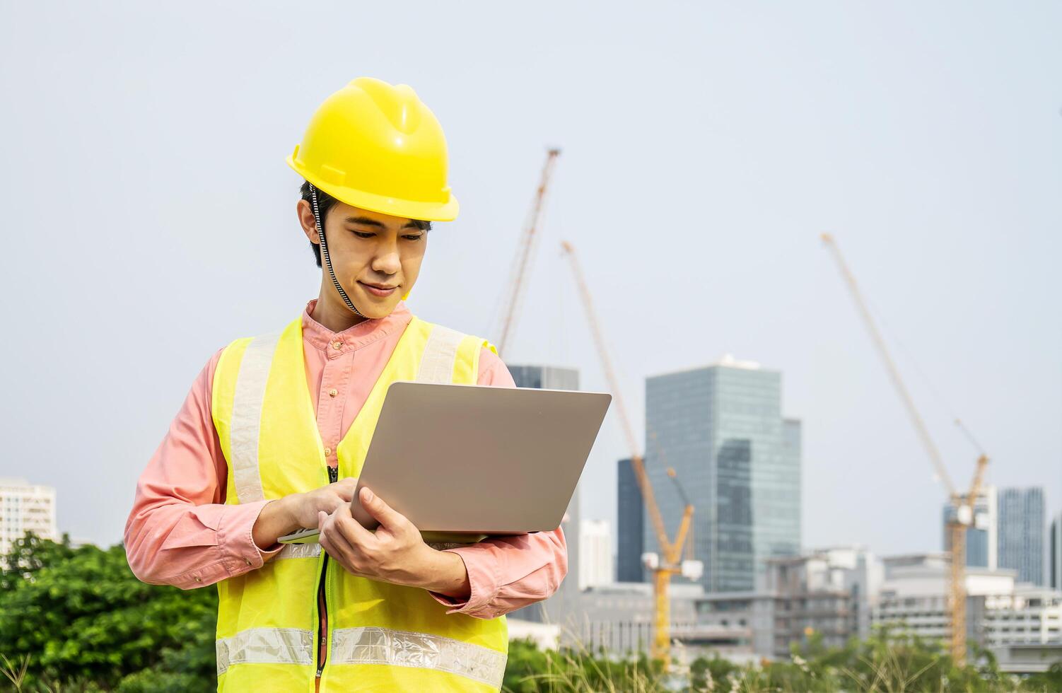 Engineer or construction worker Asian man is holding the laptop and working concentrated at building plan, Hard hat help protect with operation photo